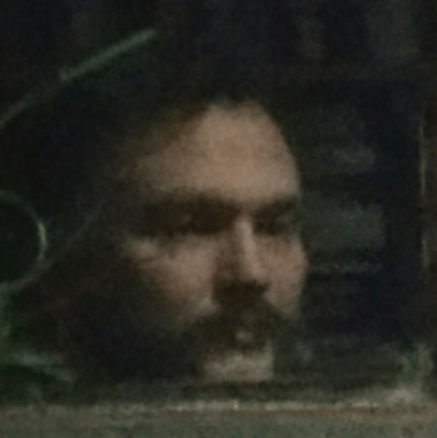 Author photo thru an old window close up of contemplative expression.