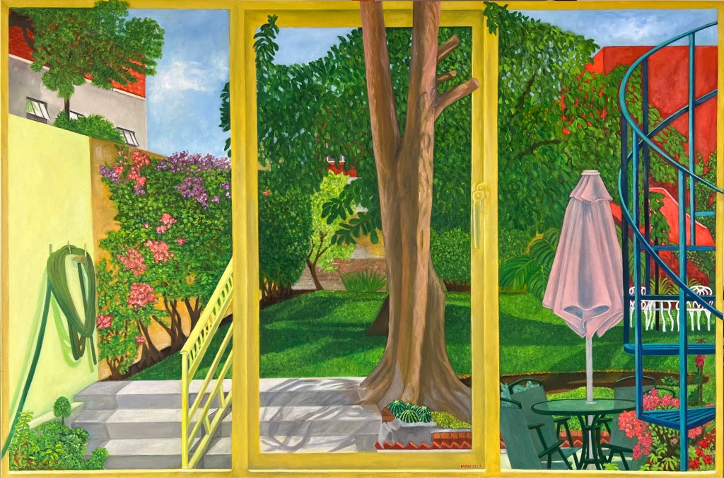 A lush green garden seen through yellow painted windows, patio doors, yellow and umber wall at left, red building behind, a large tree in front of the window-door, a pink-blue awning for a lawn table, chairs, trees and flowers -- a subtle complex vision of peace, a sealed garden, verging on surreal.