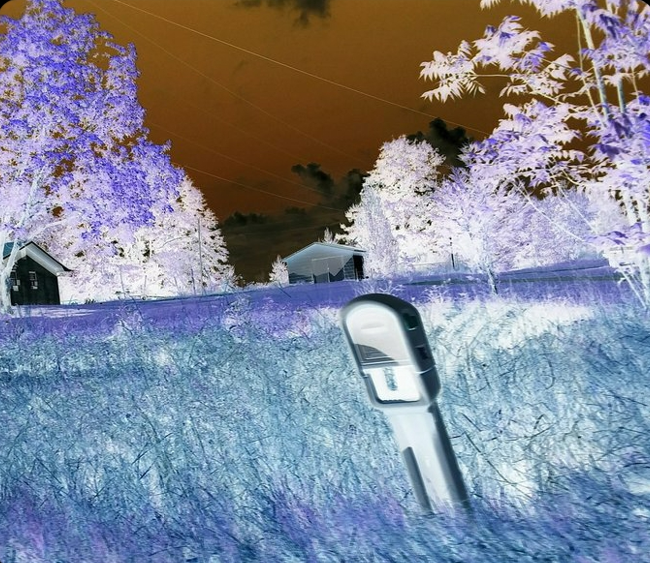 A photo / vispo work blues, purples.  a tea-stained sky, field, trees, a black ghostly house in the left side half way up the image, a foregrounded silver power box. Diagonals, sense of movement, power lines.   A photo work by Moira J. Saucer entitled Power Box, Rural Alabama.