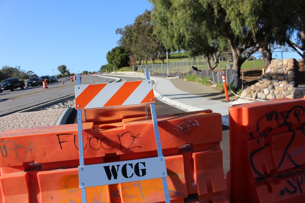 A photo of a road, a barrier (orange)  trees and a park near the ocean.  By Chantal B.