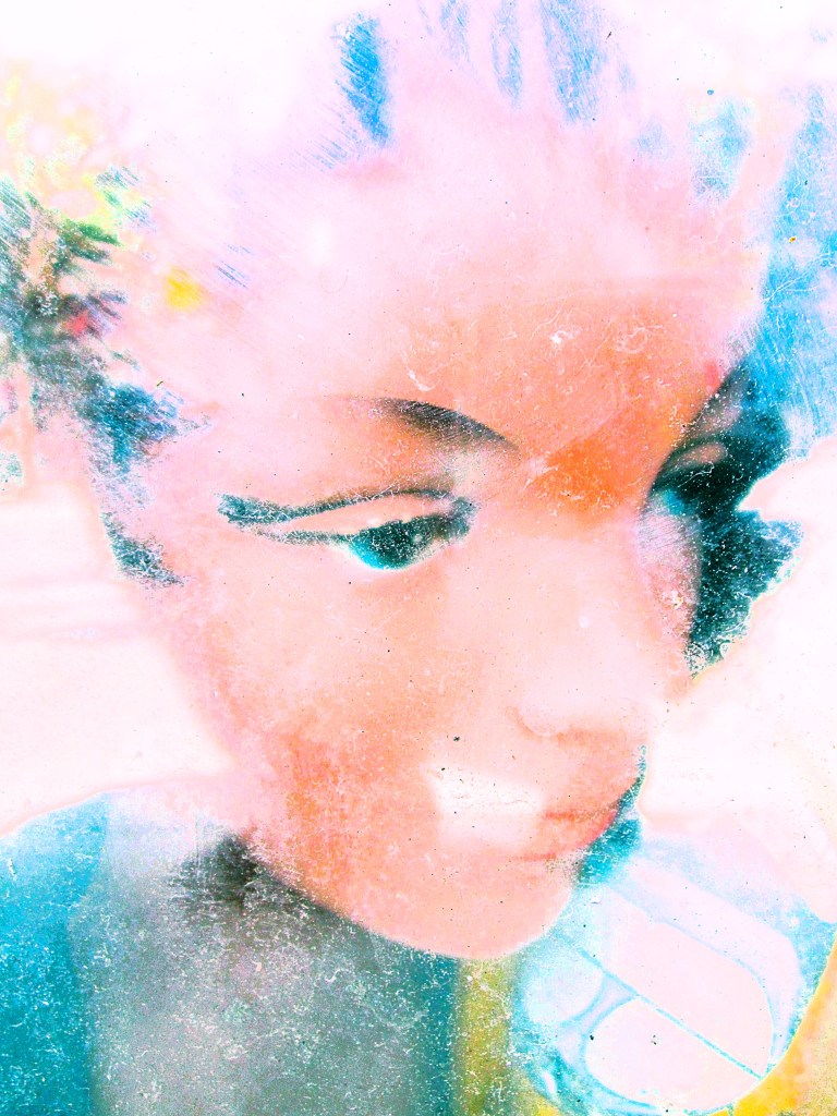 Doll, a vispo by Robert Frede Kenter. A bright fleshy coloured doll profile against pink blue and yellow pastels, blurry and looking to the side. (c) 2026